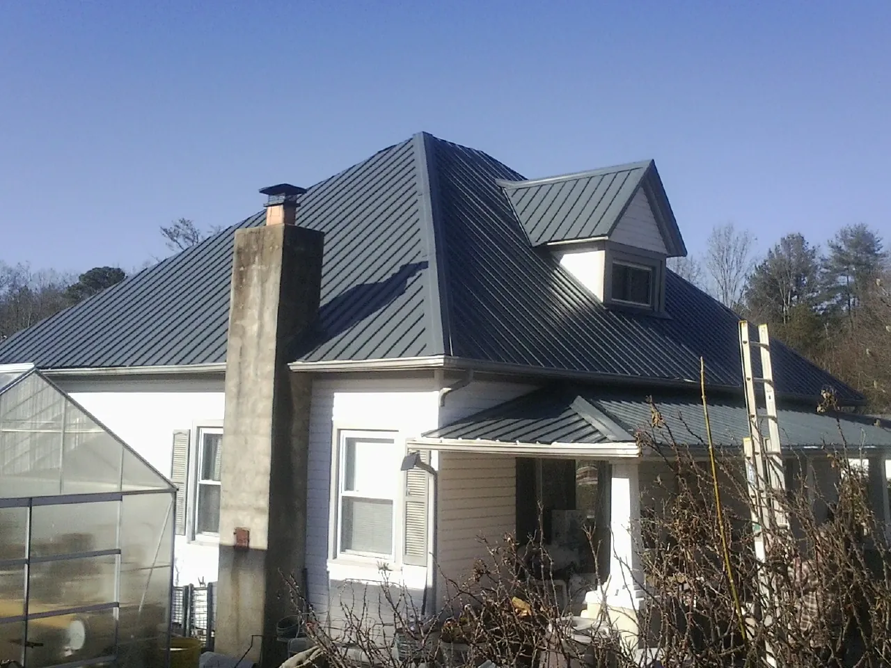 Dark blue standing seam metal roof on a white farmhouse with dormer — Slate & Tile Roof Repair by Roofing Brothers in Utica