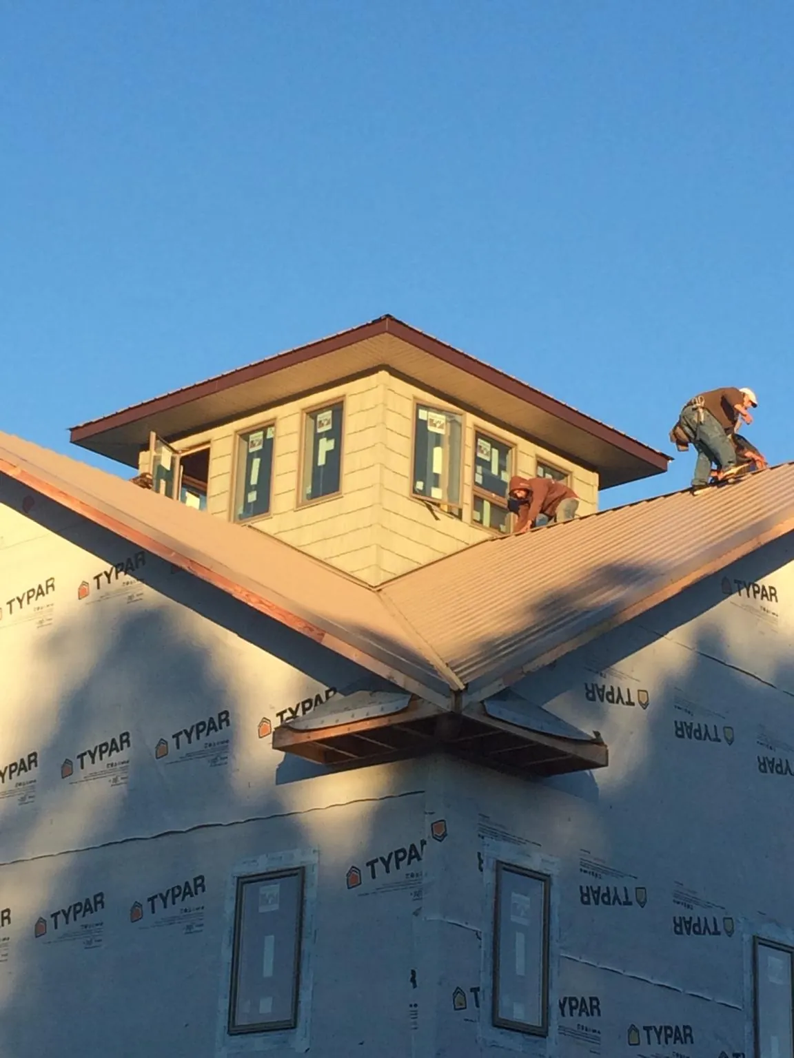 Roofers working around a rooftop cupola on a new metal roof at sunset — Roof Waterproofing in Utica by Roofing Brothers